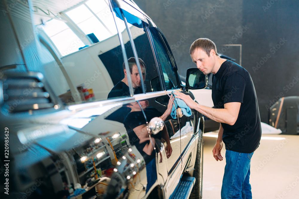 The man is wiping with a cloth body of a brilliant car. The man is wiping with a cloth body of a brilliant car.