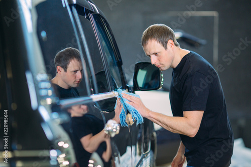 The man is wiping with a cloth body of a brilliant car.