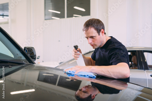 The man is wiping with a cloth body of a brilliant car.