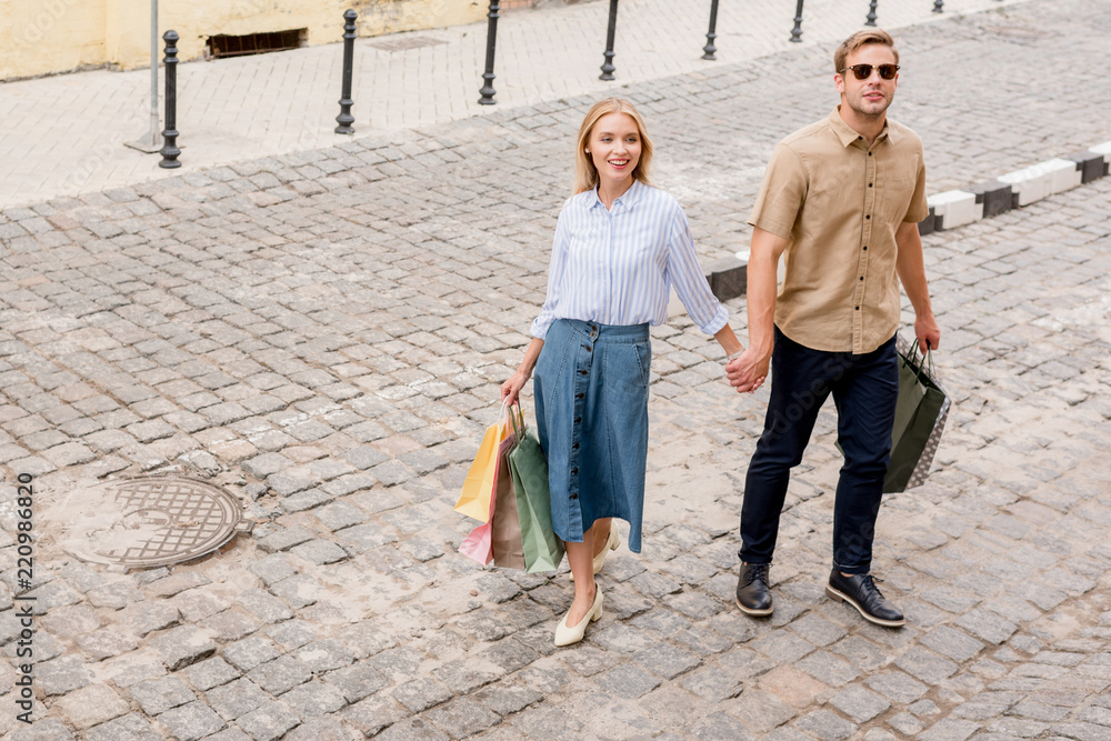 high angle view of stylish couple of shoppers with paper bags walking at city street