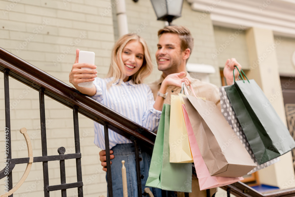 smiling young couple with paper bags taking selfie on smartphone near store at city street smiling young couple with paper bags taking selfie on smartphone near store at city street