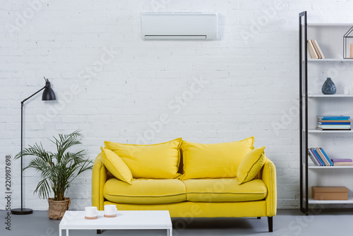 interior of modern living room with yellow couch and air conditioner hanging on white wall