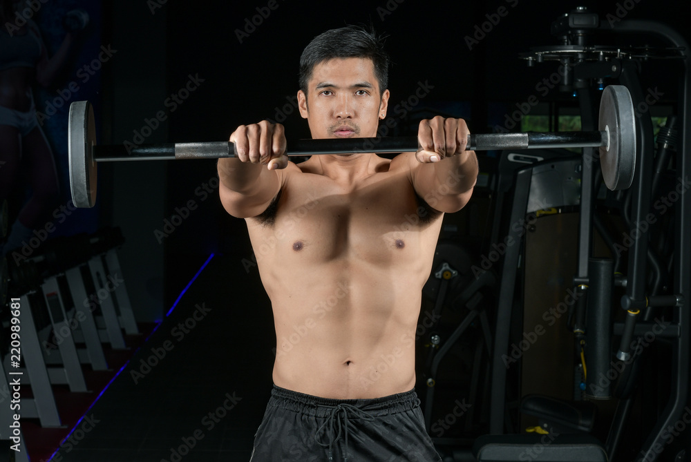 Muscular builder man training his body with barbell in Modern fitness center Muscular builder man training his body with barbell in Modern fitness center