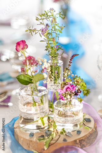 Very bright blurred flower decoration with pink roses, gypsophila and glass vases on a wooden disc
