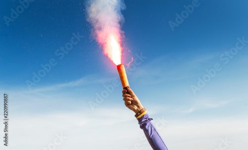 A woman in the wild mountains gives a distress signal SOS using Falsch feuer torch from which comes a bright flame and orange smoke, Concept of emergency situation during hike in the woods photo