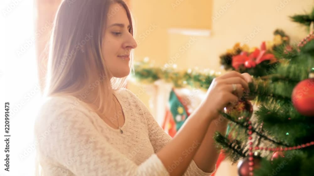 Portrait of beautiful smiling woman decorating Christmas tree in living room with colorful baubles and beads Portrait of beautiful smiling woman decorating Christmas tree in living room with colorful baubles and beads