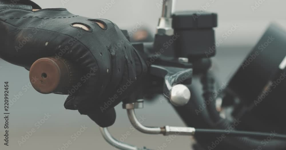Motorbike handle grips. Close up the hand of the motorcyclist holds the trottle and pushes the brake lever. The biker inserts the key into the ignition lock and turns the bike. Motorbike handle grips. Close up the hand of the motorcyclist holds the trottle and pushes the brake lever. The biker inserts the key into the ignition lock and turns the bike.