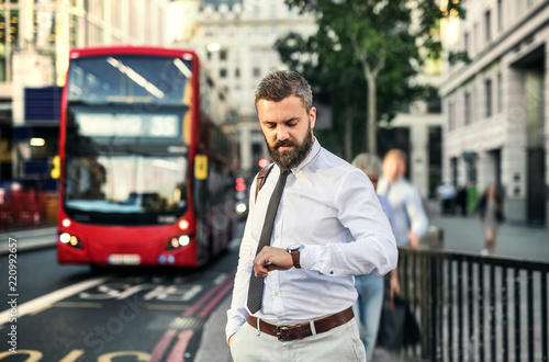 Hipster businessman waiting for the bus in London, checking the time.