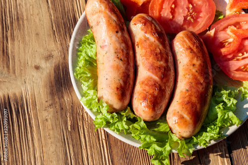 Grilled sausages with fresh vegetables on wooden table