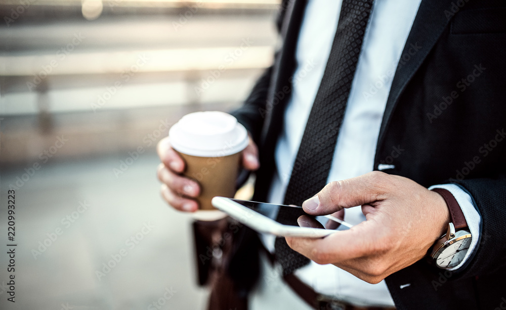 A close-up of a businessman with smartphone and coffee in the city, texting.