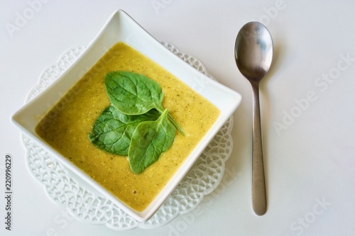 Tasty spinach soup bowl on the white table with spoon.