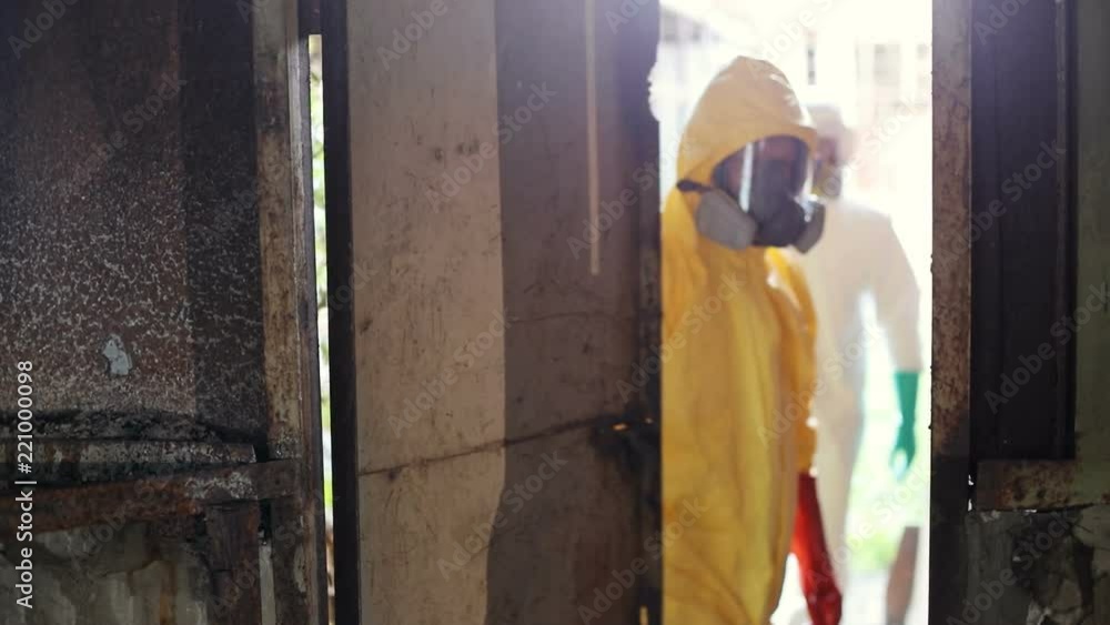 Young Caucasian man in yellow hazmat outfits and respirator mask. Slavic guy looking round and going through the door. Old building. Indoors. Young Caucasian man in yellow hazmat outfits and respirator mask. Slavic guy looking round and going through the door. Old building. Indoors.