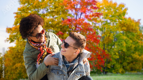 leisure, people and season concept - happy mixed race teenage couple having fun over autumn park background