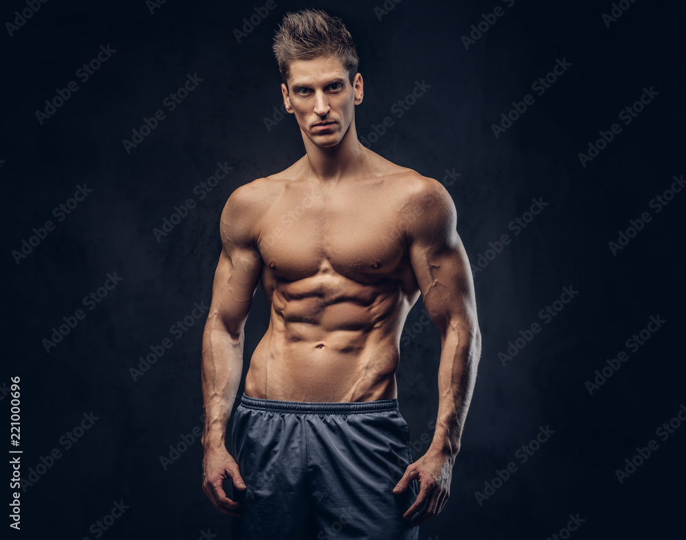 Fototapeta premium Handsome shirtless ectomorph bodybuilder with stylish hair posing on a dark background.