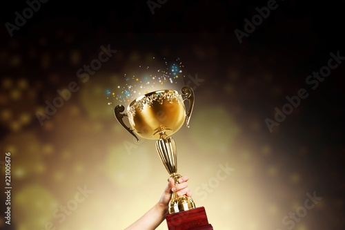 Close-up human hand holding golden Trophy on blurred background
