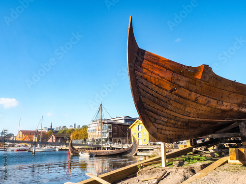 Old retro wooden viking vessel at harbor, against blue sky and blue water