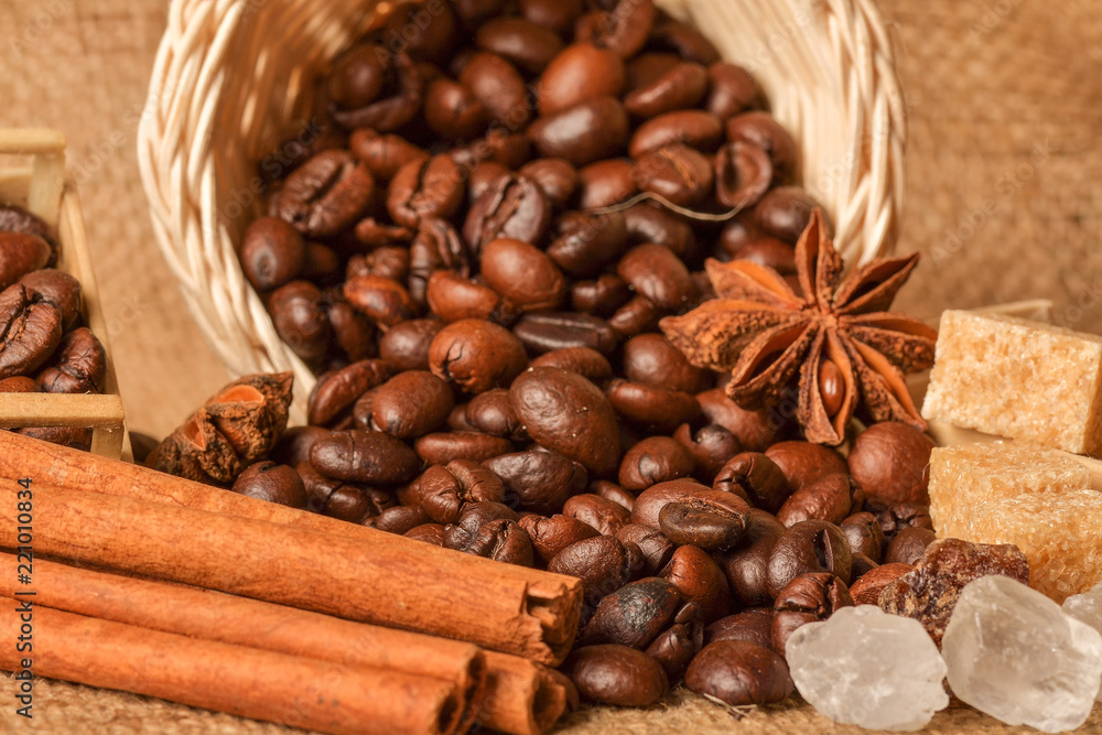 Coffee beans and cinnamon on a background of burlap. Roasted coffee beans background close up. Coffee beans pile from top with copy space for text. Seasoning. Spice. Cinnamon. Badian. Coffee house.