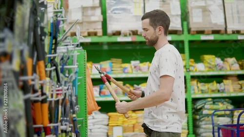 Brunet customer choosing garden tools in a hardware store, holding big clipper with wooden handels. Gardening tools in a store, male customer. photo