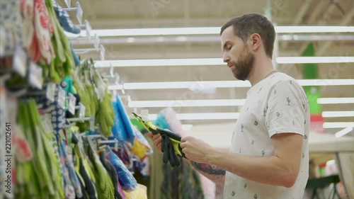 Man is groping rubber gloves for gardening works in a shop. He is touching and checking materials of goods