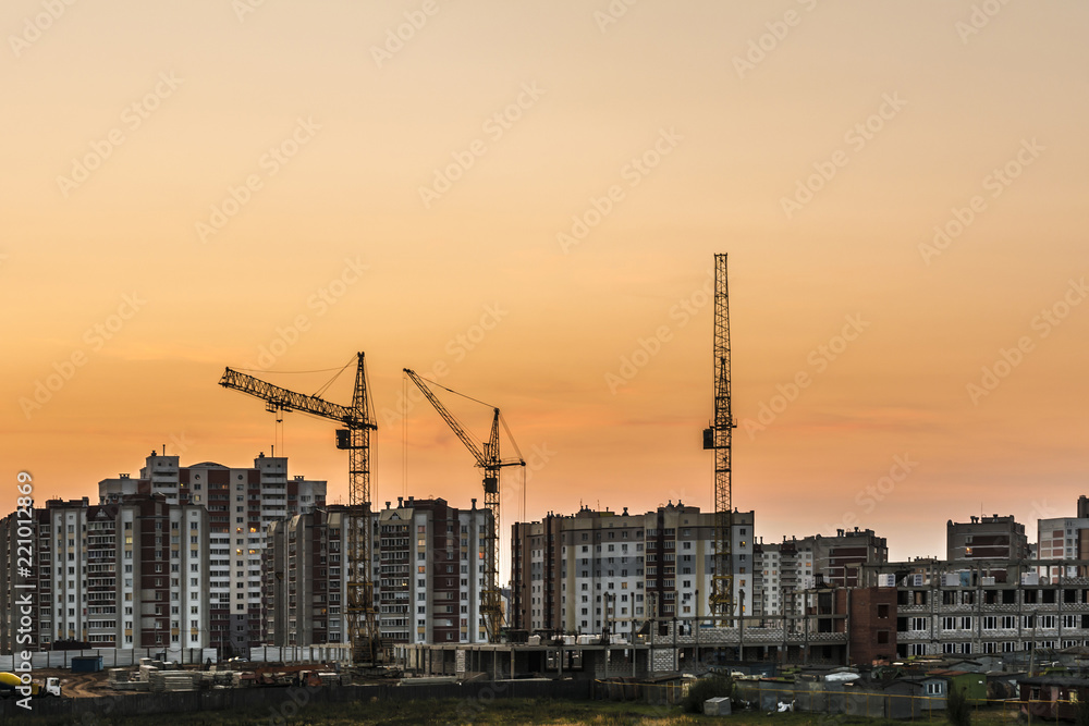 building site with three tower cranes against the background of multi-storey houses and a orange sky, night scene