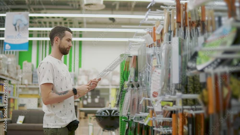 Man is choosing grill lattice in a hypermarket. He is taking it from rack, disassembling it and inspecting Man is choosing grill lattice in a hypermarket. He is taking it from rack, disassembling it and inspecting