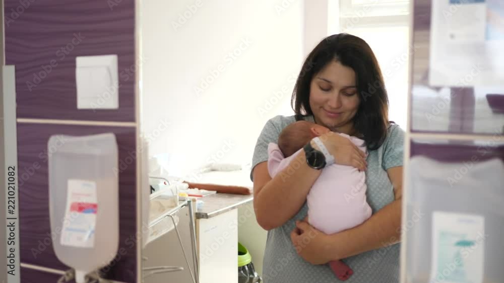Woman mother holds and kiss her newborn baby girl in maternity hospital room mirror Woman mother holds and kiss her newborn baby girl in maternity hospital room mirror