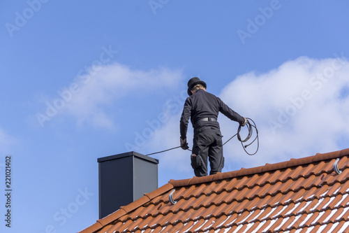 Billede på lærred Chimney sweep cleaning a chimney standing on the house roof, lowering equipment
