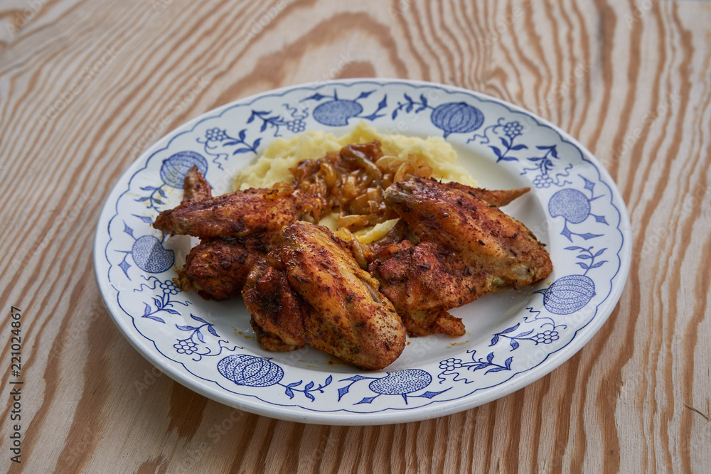 Close up Picture of old rustic plate with roasted spicy chicken hot wings, mashed potatoes as a side dish with glazed, baked or fried onions on wooden table background. Close up Picture of old rustic plate with roasted spicy chicken hot wings, mashed potatoes as a side dish with glazed, baked or fried onions on wooden table background.