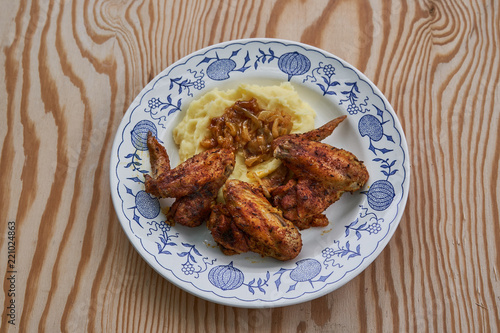 Close up Picture of old rustic plate with roasted spicy chicken hot wings, mashed potatoes as a side dish with glazed, baked or fried onions on wooden table background.