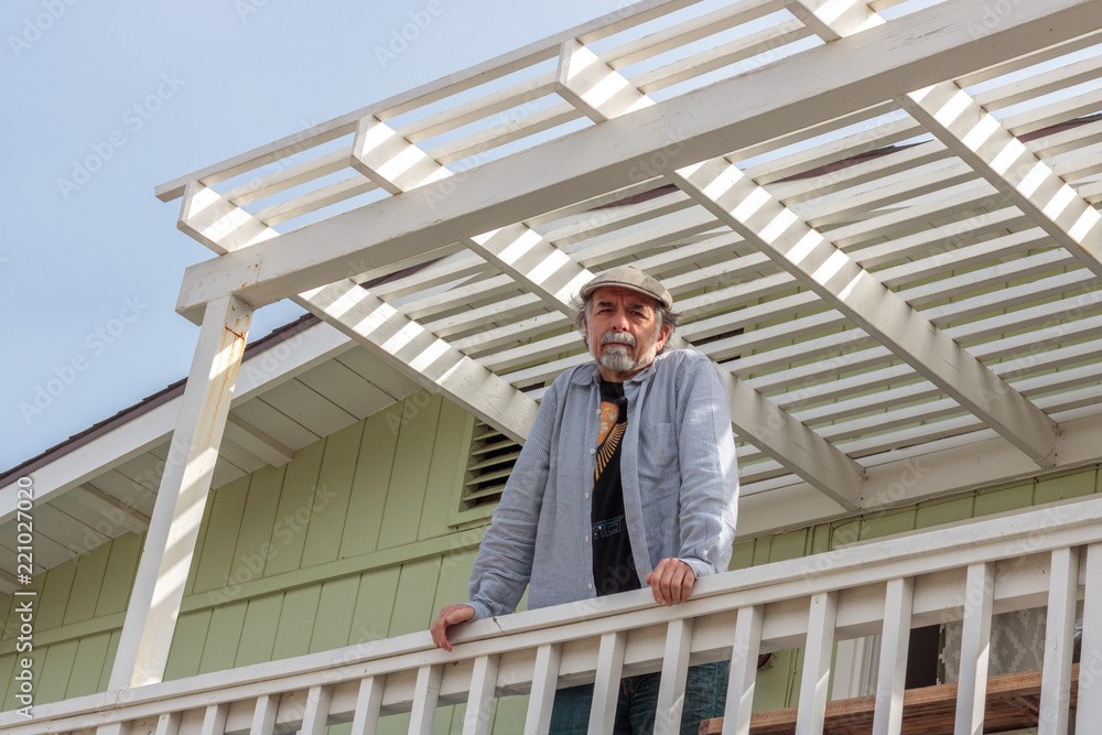 Senior, white male with gray beard looking down at camera from above on a white deck in the sun light Senior, white male with gray beard looking down at camera from above on a white deck in the sun light