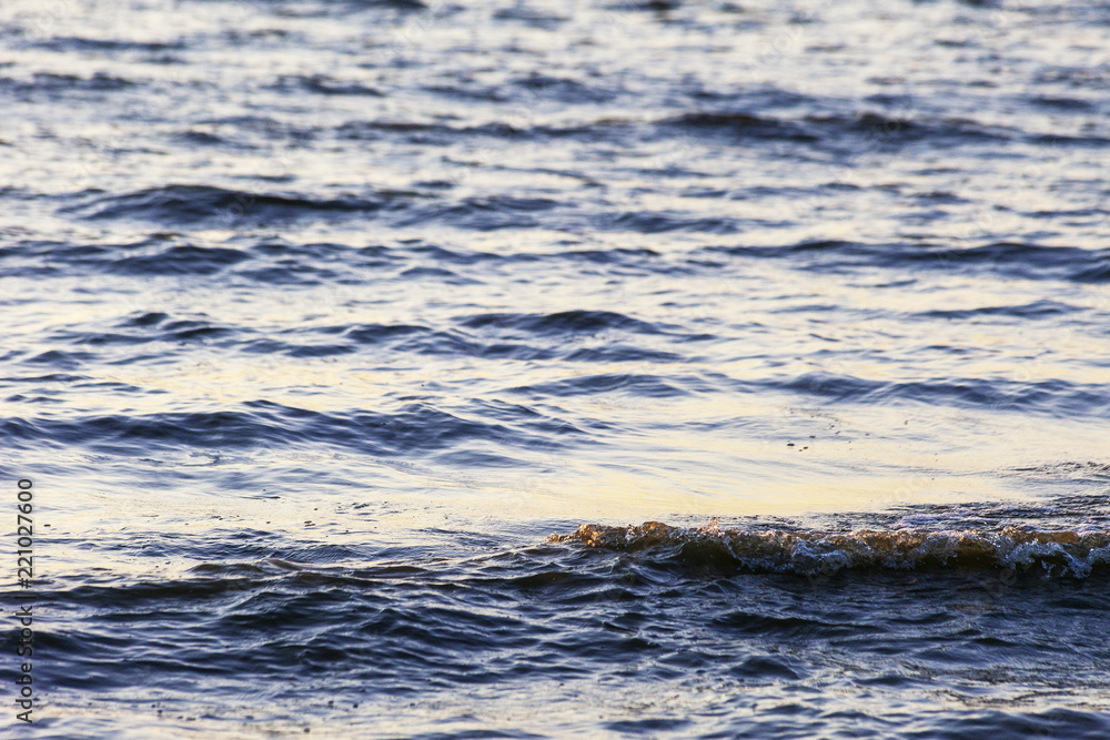 Waves on the sandy shore of a large river. The rays of light are reflected in the waves. Waves on the sandy shore of a large river. The rays of light are reflected in the waves.
