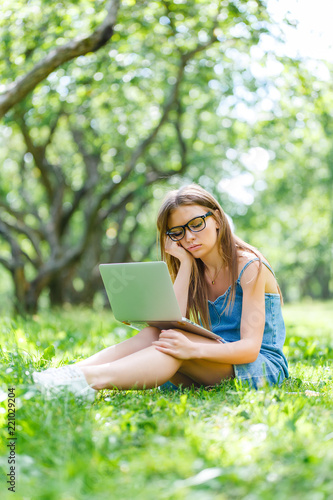 Young woman with notebook in park looking at laptop
