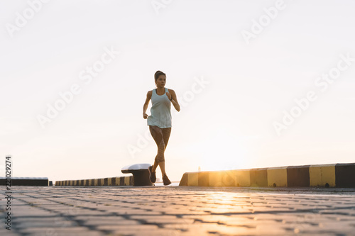 Side view of fitness woman running on a road by the sea. Sportswoman training on seaside promenade at sunset.