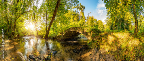 Photographie Old bridge over a creek in the forest with bright sun shining throug the trees