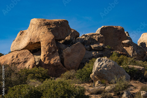 Southwest desert landscape, blue sky, desert plants, yucca and large boulders in foreground,