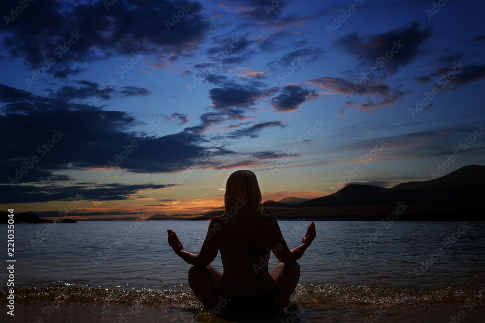 Silhouette of woman practicing yoga relaxation at sunset by the sea 