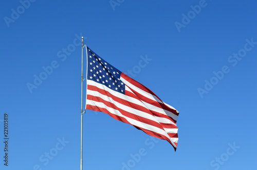 Large American flag waving in the wind with a clear blue sky background