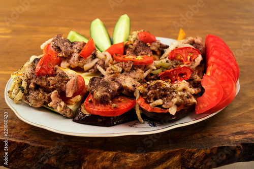 Meat dish with baked eggplant, tomato, zucchini and onion, wooden background.