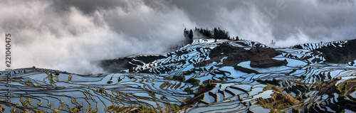Yuanyang Rice Terraces in Yunnan Province, China - Early morning photograph with reflection of the sky causing water in the terraces to appear blue. Mist in the background, Duoyishu landscape, clouds