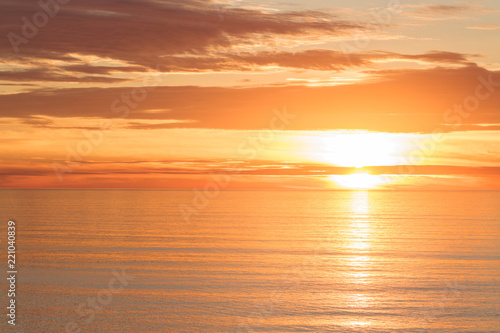 Bright golden dramatic sunset sun reflecting orange, gold, off calm ocean