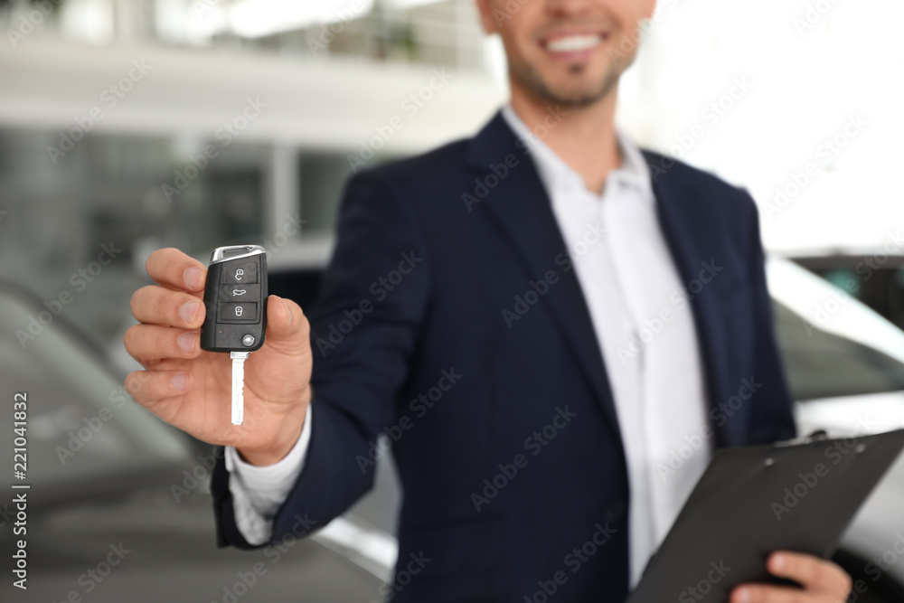 Salesman with clipboard and car key standing in salon Salesman with clipboard and car key standing in salon