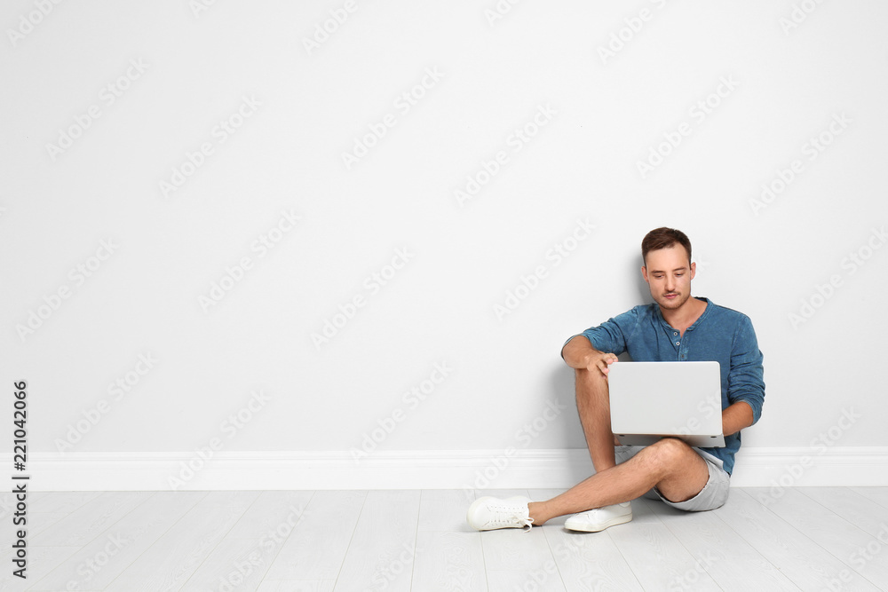 Young man with laptop sitting on floor against light wall. Space for text Young man with laptop sitting on floor against light wall. Space for text