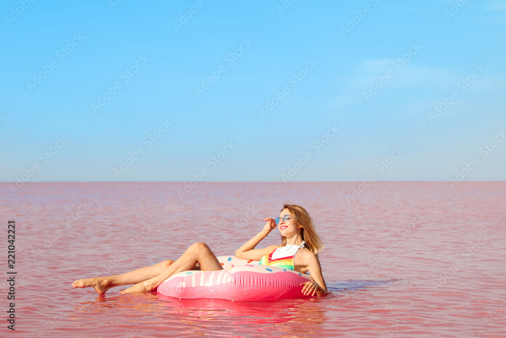 Naklejka premium Beautiful woman on inflatable ring in pink lake