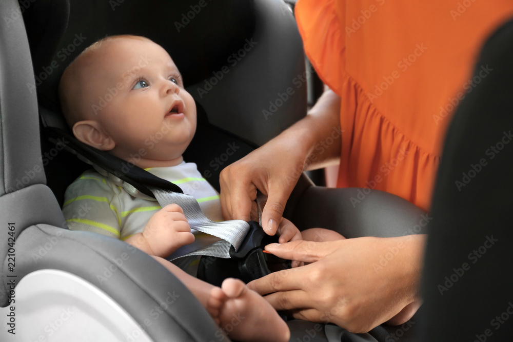 Mother fastening baby to child safety seat inside of car Mother fastening baby to child safety seat inside of car