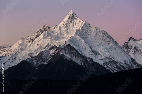 Meilixueshan - Meili Snow Mountain range in Deqin, Yunnan Province China. Early Dawn view of exotic China mountains, vibrant pink and purple atmospheric sky. Crisp white snow cliffs and glaciers