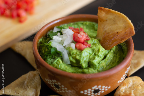 Guacamole mexicano tradicional de la salsa en el cuenco de arcilla y nachos en el fondo de un tablero de pizarra