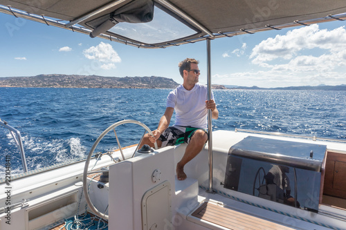 Attractive male skipper navigating the fancy catamaran sailboat on sunny summer day on calm blue sea water. Luxury summer adventure, active nautical vacation. photo