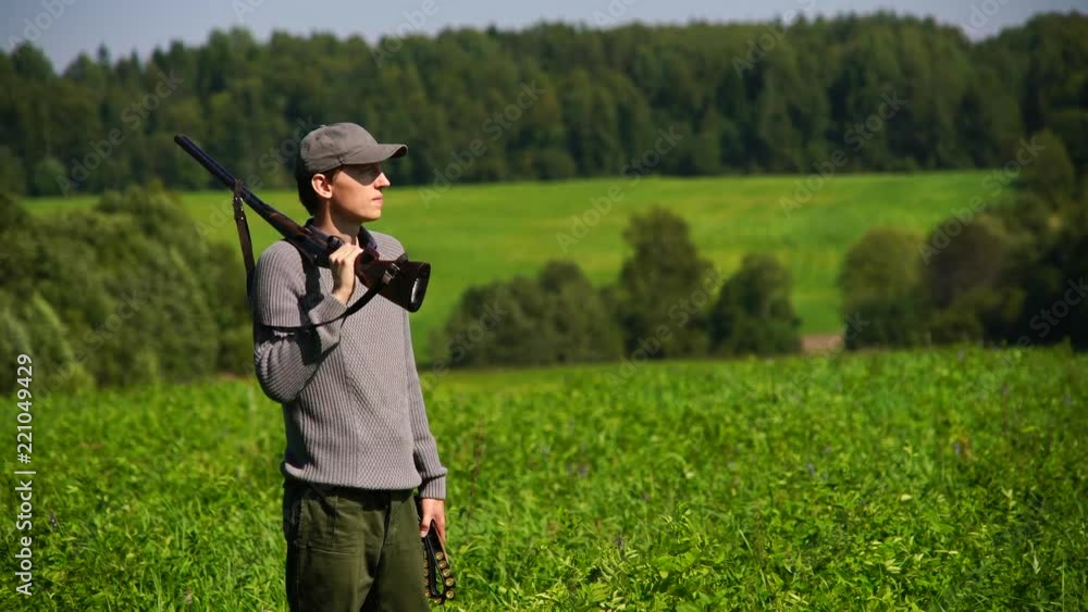 A hunter with a hunting gun stands in the field and looks around. A hunter with a hunting gun stands in the field and looks around.