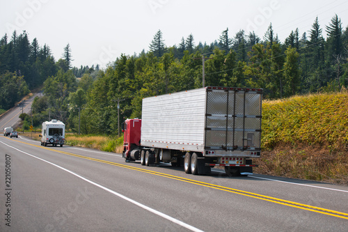 Red big rig cab-over semi truck transporting cargo in refrigerator semi trailer on the hills road © vit