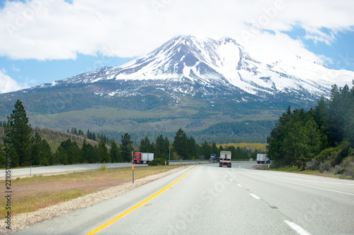 Wide multi - lines highway road with big rig semi trucks driving downhill and uphill with snowy mountain view